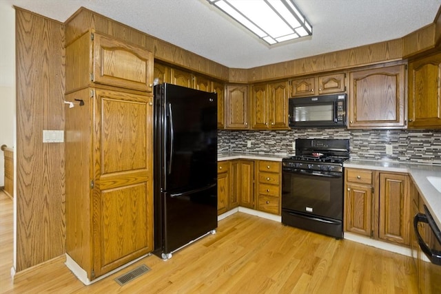 kitchen featuring visible vents, tasteful backsplash, brown cabinets, light countertops, and black appliances