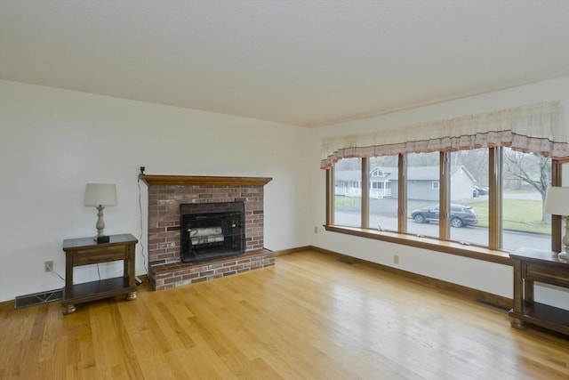 unfurnished living room featuring baseboards, a brick fireplace, wood finished floors, and visible vents