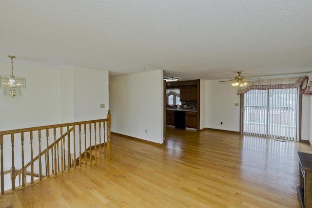 spare room featuring baseboards, ceiling fan with notable chandelier, and light wood-style flooring