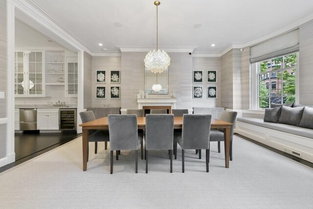 dining area featuring a large fireplace, light wood-type flooring, ornamental molding, an inviting chandelier, and wine cooler