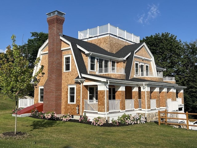 back of house with a balcony, a lawn, a gambrel roof, and roof with shingles