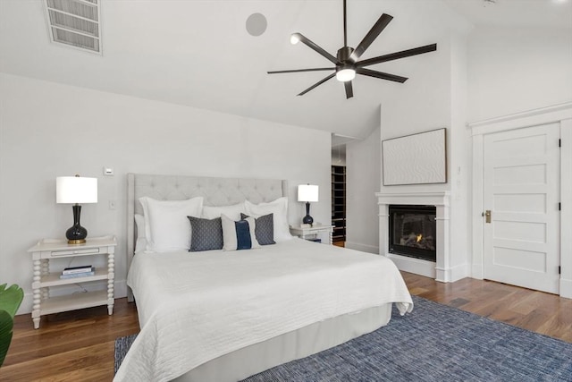 bedroom featuring a glass covered fireplace, vaulted ceiling, wood finished floors, and visible vents