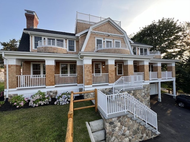 shingle-style home with covered porch, a chimney, stairs, and a gambrel roof