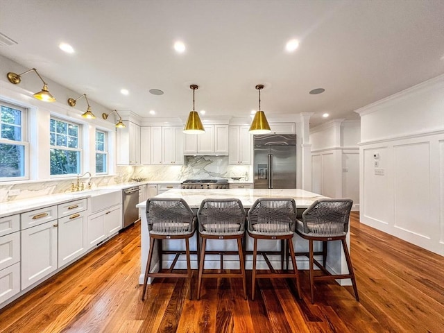 kitchen featuring wood finished floors, light stone countertops, a kitchen island, appliances with stainless steel finishes, and tasteful backsplash