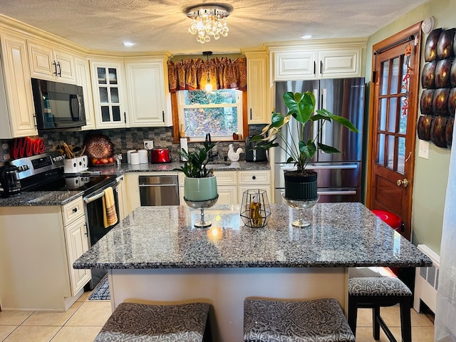 kitchen featuring a kitchen breakfast bar, appliances with stainless steel finishes, dark stone counters, and a center island