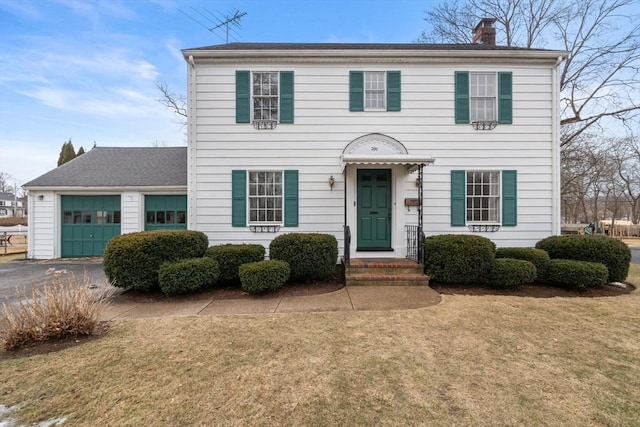 colonial inspired home with a front yard, an attached garage, driveway, and a chimney