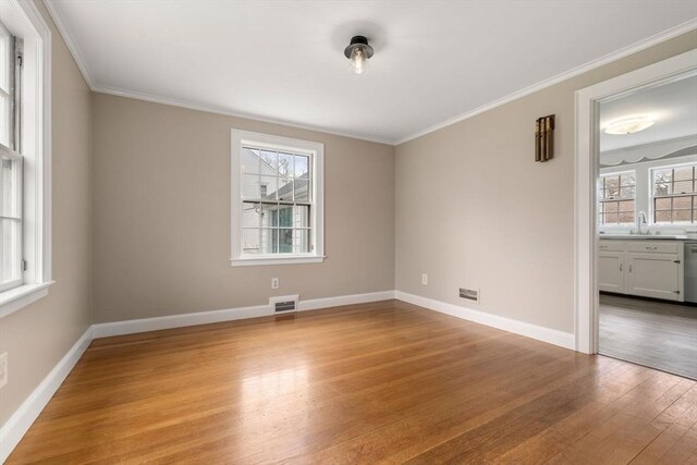 unfurnished room featuring wood finished floors, a healthy amount of sunlight, visible vents, and ornamental molding