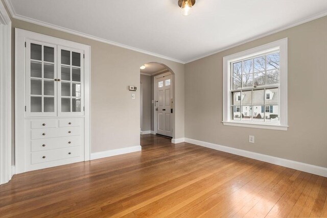 spare room featuring crown molding, hardwood / wood-style flooring, baseboards, and arched walkways