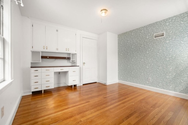 interior space with built in desk, wallpapered walls, light wood-type flooring, and visible vents