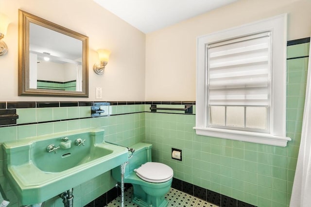 bathroom with a sink, a wainscoted wall, toilet, and tile walls