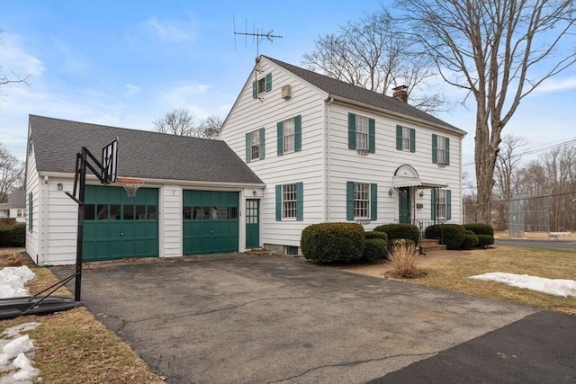 colonial-style house featuring driveway, an attached garage, roof with shingles, and a chimney