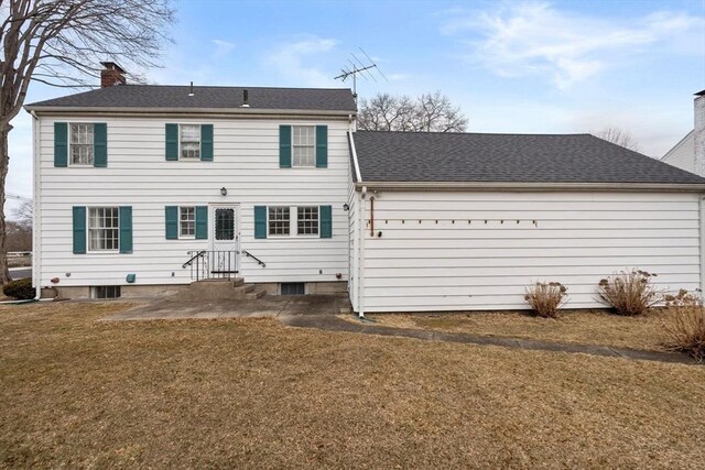 rear view of house with a lawn, a shingled roof, a chimney, and entry steps