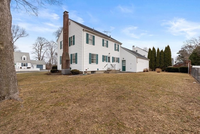 rear view of property with a lawn, entry steps, a chimney, and fence