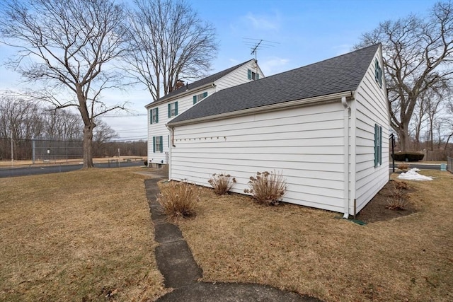 view of property exterior featuring a shingled roof, a yard, and fence