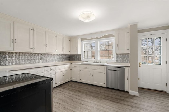 kitchen featuring light wood finished floors, a sink, decorative backsplash, light countertops, and stainless steel dishwasher