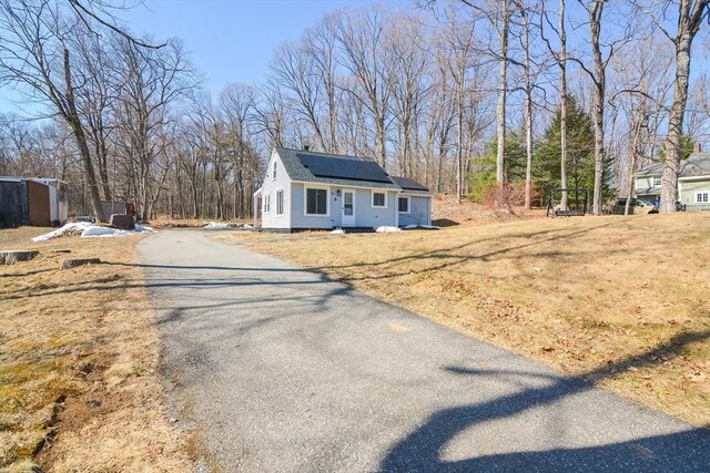 view of front of property featuring aphalt driveway, solar panels, and a front yard