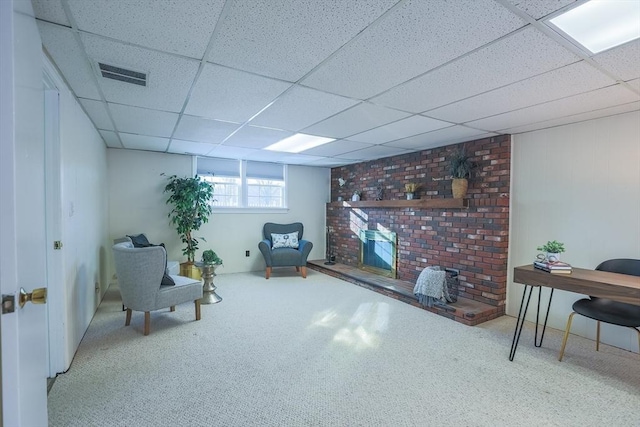 living area featuring a fireplace, a drop ceiling, and carpet