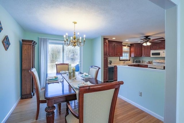 dining area with sink, ceiling fan with notable chandelier, light hardwood / wood-style flooring, and a textured ceiling