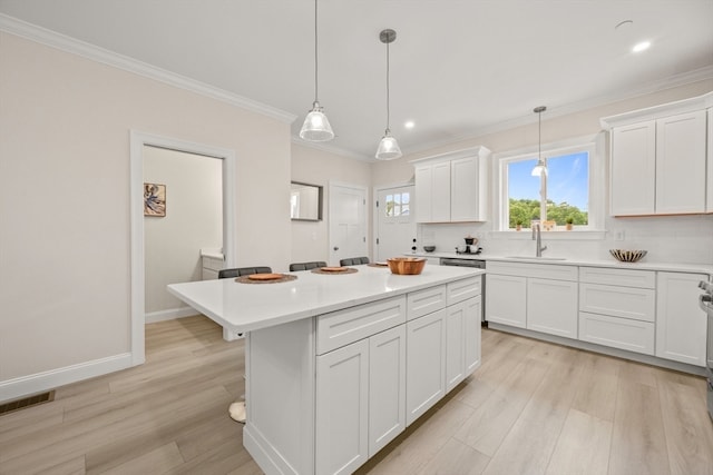 kitchen with sink, white cabinets, hanging light fixtures, a kitchen island, and light hardwood / wood-style flooring