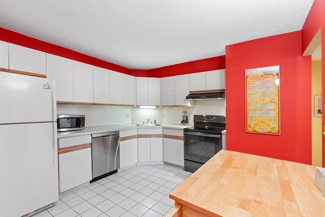 kitchen with appliances with stainless steel finishes, under cabinet range hood, white cabinetry, light tile patterned floors, and a sink