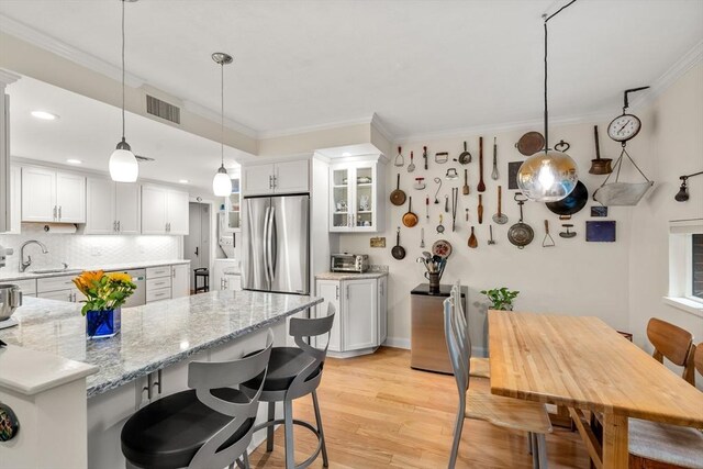kitchen featuring a breakfast bar, crown molding, white cabinetry, visible vents, and appliances with stainless steel finishes