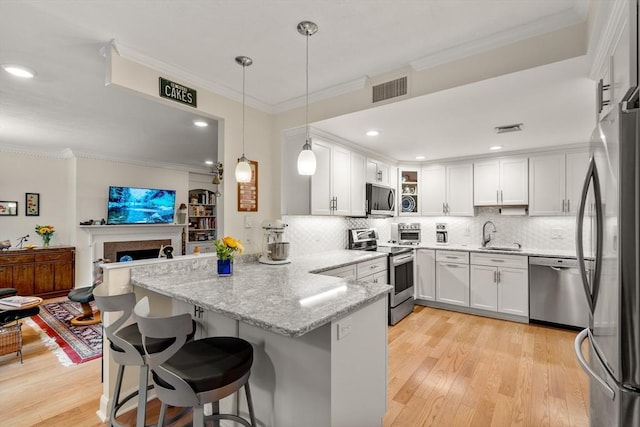 kitchen with ornamental molding, visible vents, a sink, a peninsula, and appliances with stainless steel finishes