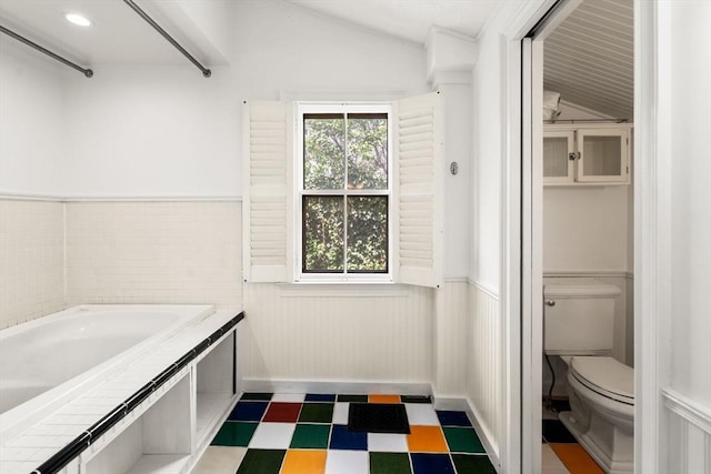 bathroom with tile patterned floors, a wainscoted wall, toilet, and vaulted ceiling