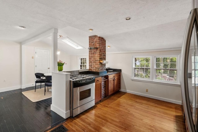 kitchen with stainless steel range with gas cooktop, vaulted ceiling, baseboards, hardwood / wood-style floors, and a peninsula