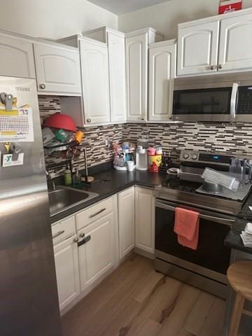 kitchen featuring backsplash, wood-type flooring, appliances with stainless steel finishes, and white cabinetry