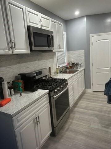 kitchen with light hardwood / wood-style floors, sink, stainless steel appliances, white cabinets, and light stone counters