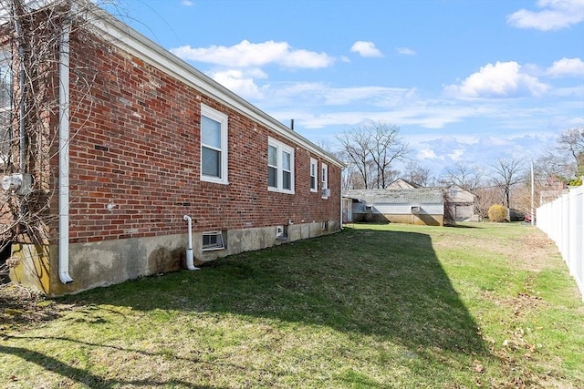 view of side of property with a lawn, fence, and brick siding