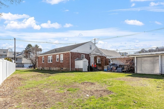 back of property with an outbuilding, a yard, brick siding, a storage unit, and fence