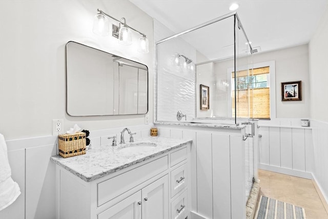 bathroom featuring vanity, a shower with shower door, a wainscoted wall, and tile patterned flooring