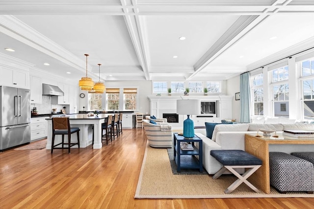 living area featuring beam ceiling, light wood-style flooring, a fireplace, and a wealth of natural light