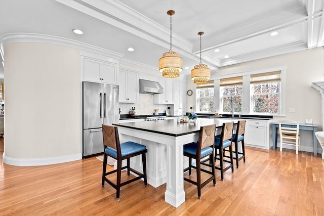 kitchen with a breakfast bar, dark countertops, light wood-style floors, wall chimney range hood, and high end refrigerator