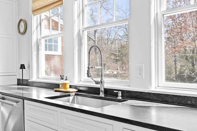 kitchen with a sink, dark countertops, dishwasher, and white cabinetry