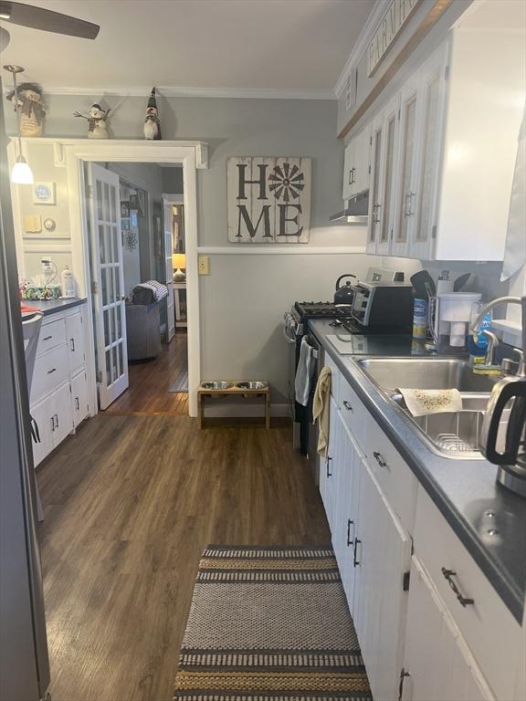 kitchen with dark wood-style floors, dark countertops, ornamental molding, white cabinetry, and a sink