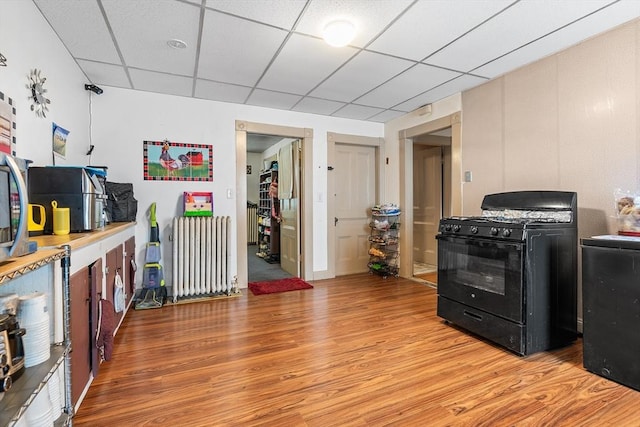 kitchen featuring radiator heating unit, light hardwood / wood-style flooring, a drop ceiling, and black range with gas cooktop