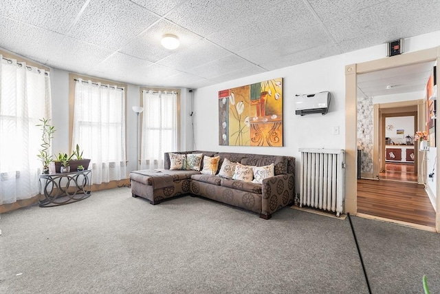 living room with a paneled ceiling, carpet, radiator, and a wall mounted AC