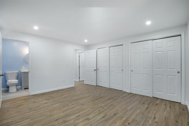 unfurnished bedroom featuring connected bathroom, two closets, baseboards, recessed lighting, and wood finished floors