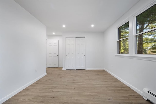 unfurnished bedroom featuring baseboards, baseboard heating, recessed lighting, light wood-style flooring, and a closet