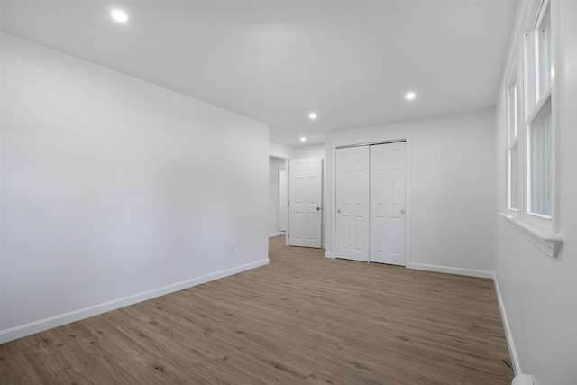 unfurnished bedroom with a closet, recessed lighting, baseboards, and wood finished floors