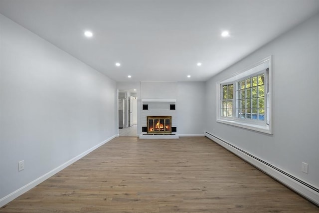 unfurnished living room featuring wood finished floors, baseboards, recessed lighting, a glass covered fireplace, and baseboard heating