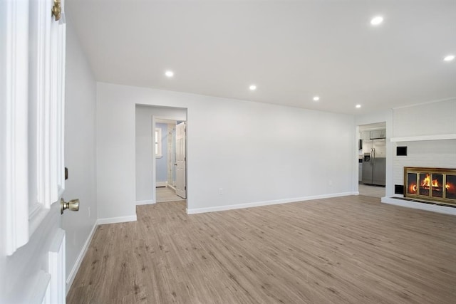 unfurnished living room featuring recessed lighting, baseboards, light wood-style floors, and a brick fireplace