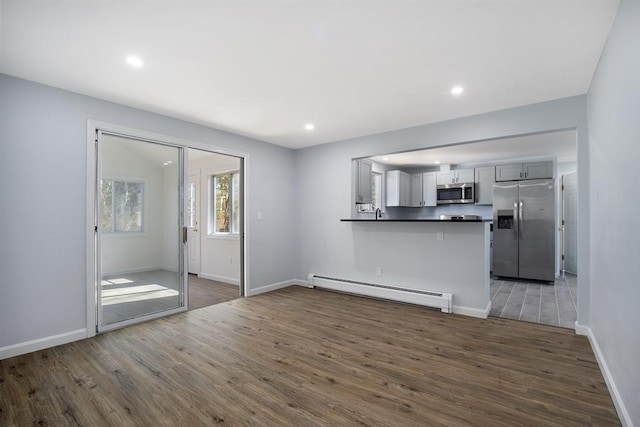 unfurnished living room featuring recessed lighting, a baseboard radiator, baseboards, and wood finished floors