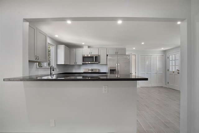 kitchen with dark countertops, recessed lighting, appliances with stainless steel finishes, a peninsula, and light wood finished floors