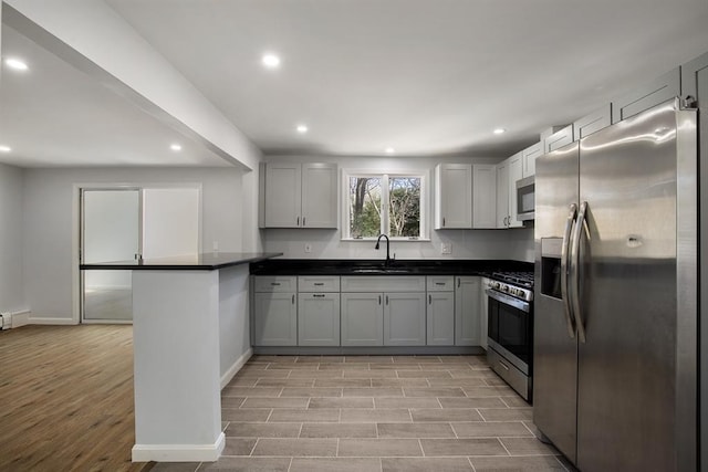 kitchen featuring dark countertops, wood finish floors, a peninsula, stainless steel appliances, and a sink