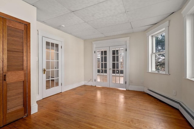 unfurnished room with baseboards, a baseboard radiator, hardwood / wood-style flooring, a paneled ceiling, and french doors