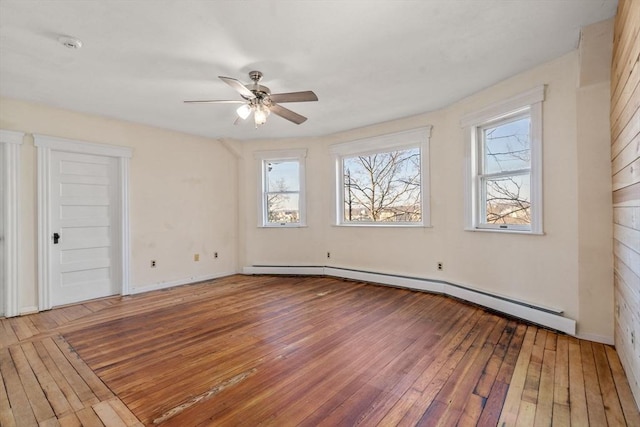 unfurnished room with a baseboard heating unit, a ceiling fan, baseboards, and wood-type flooring