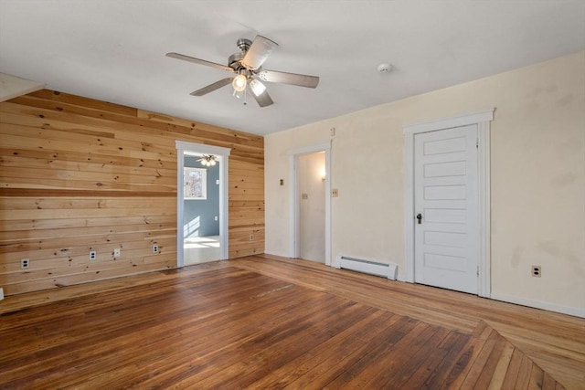 spare room featuring ceiling fan, hardwood / wood-style flooring, wood walls, and a baseboard radiator